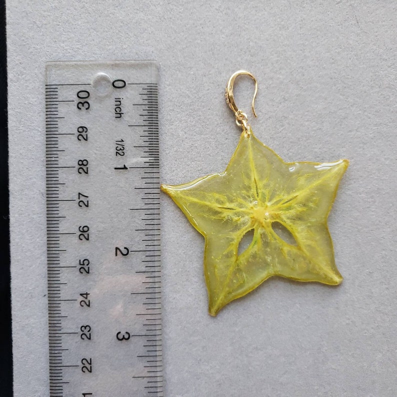 May include: A single starfruit earring with a gold-colored hook. The earring is a translucent yellow color, with a star shape. The earring measures approximately 2.5 inches in length.