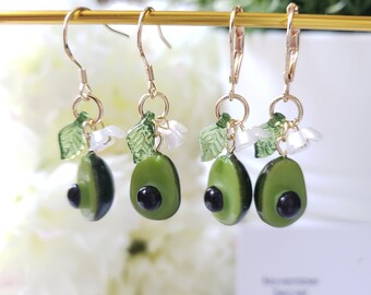 May include: Three pairs of gold avocado earrings with green leaves and white pearl accents.