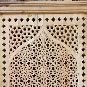 May include: A wooden panel with intricate carved geometric designs in a light wood tone. The design features a repeating pattern of stars and circles.