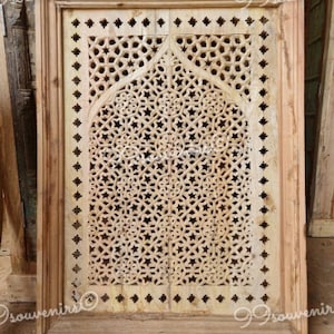 May include: A wooden windowpane with a carved geometric design. The design features a repeating pattern of stars and circles, creating a delicate and intricate look. The windowpane is framed in a simple wooden frame.