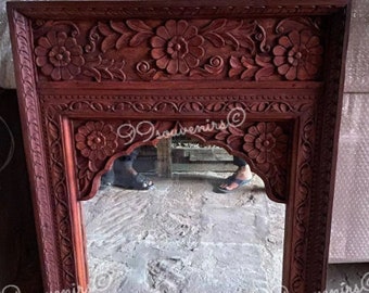 May include: A wooden mirror with a carved frame. The frame is intricately carved with floral designs and has a reddish-brown color.