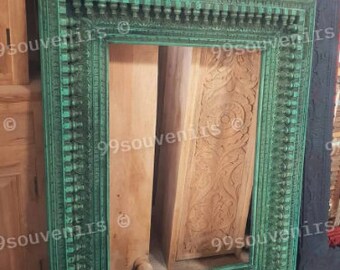 Könnte beinhalten: Ein großer, verzierter, grüner Holzbildrahmen mit aufwendigen Schnitzereien. Der Rahmen lehnt an einer Holzwand und einer Holztür.