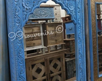 May include: A blue wooden mirror with intricate carvings and an arched top. The mirror reflects other furniture in the room.