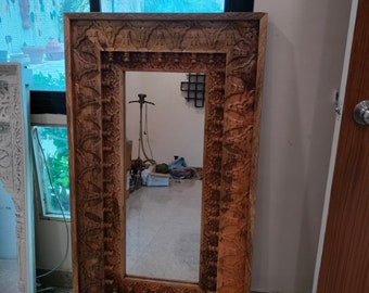 Puede incluir: Un espejo grande, rectangular de madera con un marco tallado en relieve. El marco es de color marrón oscuro y tiene detalles intrincados. El espejo en sí es transparente y refleja la habitación circundante.