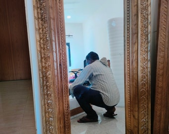 Puede incluir: Un espejo grande de madera tallada con un marco ornamentado. El marco es de color marrón oscuro y presenta detalles intrincados. El espejo refleja a una persona de pie frente a él.