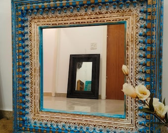 May include: A large, ornate mirror with a blue and gold frame. The frame is intricately carved with a floral design. The mirror is reflecting a room with a smaller mirror in the background.