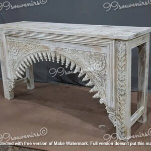 May include: White wooden console table with intricate carved details. The table features an arched design with floral motifs and a distressed finish.
