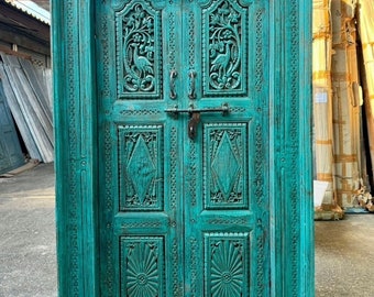 Puede incluir: Una puerta de madera turquesa con intrincadas tallas. La puerta presenta tallas en relieve detalladas de pájaros y patrones florales. Tiene un marco rectangular y un pestillo de metal. La puerta es una pieza vintage o antigua.