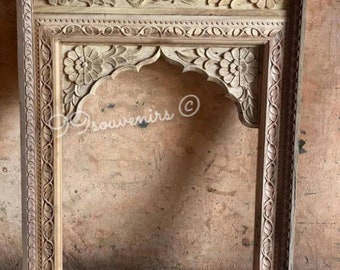 May include: A wooden frame with intricate carvings of flowers and leaves. The frame is made of light brown wood and has a rectangular shape. The frame is empty and ready to be used for a picture or mirror.