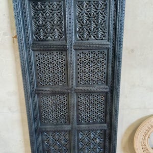 Könnte beinhalten: Eine schwarze Holztür mit aufwendigen Schnitzereien in einem geometrischen Muster. Die Tür besteht aus mehreren Paneelen mit unterschiedlichen Designs.