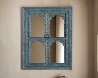 May include: A blue wooden mirror with a carved frame and four arched panels. The mirror is hanging on a beige wall.