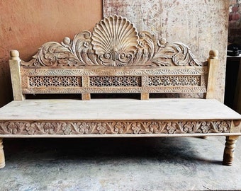 May include: A carved wooden bench with intricate details. The bench has a high back with a shell design and a lower section with a lattice pattern. The bench is made of light wood and has a natural finish.