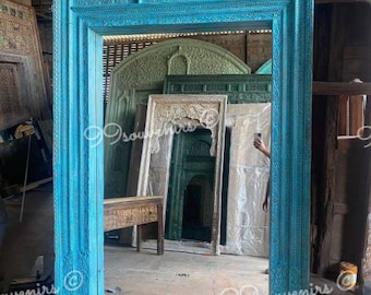 May include: A large, intricately carved wooden frame painted in a vibrant turquoise blue. The frame is designed to hold a mirror or artwork. The frame is made of reclaimed wood and has a rustic, antique look.