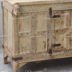 Puede incluir: Un armario de madera tallada con un acabado marr&oacute;n claro. El armario tiene dos puertas con tallas intrincadas y una parte superior decorativa.