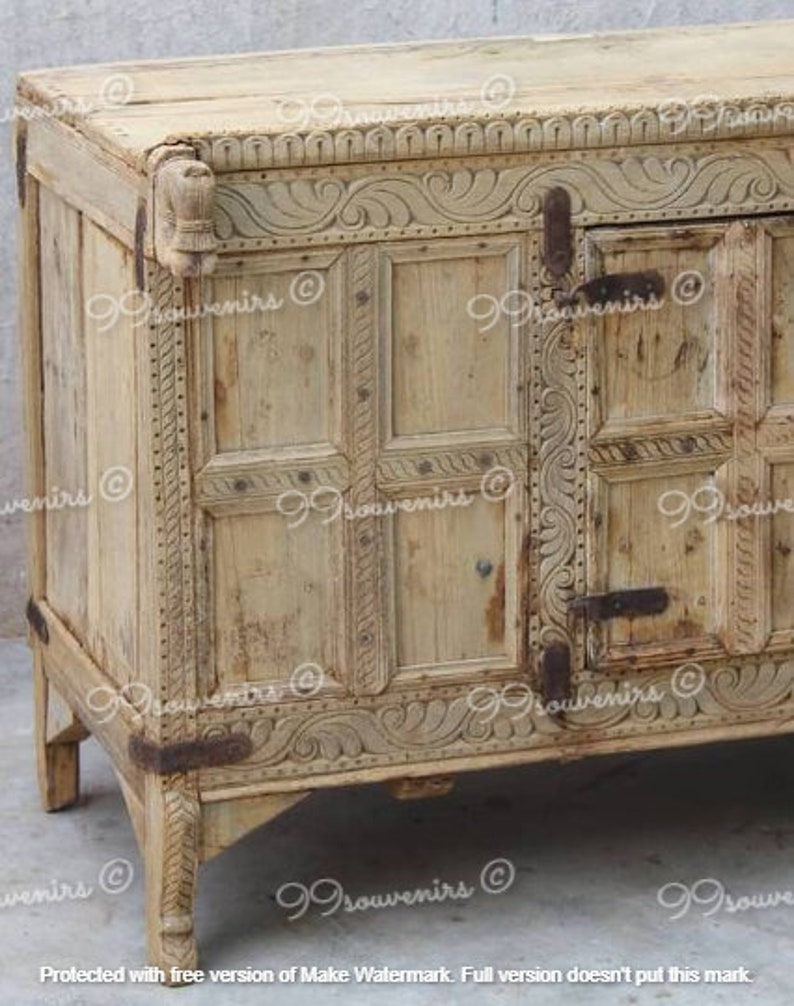 Puede incluir: Un armario de madera tallada con un acabado marr&oacute;n claro. El armario tiene dos puertas con tallas intrincadas y una parte superior decorativa.