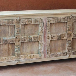 Puede incluir: Un aparador de madera blanco con tres puertas y detalles tallados intrincados. El aparador tiene un acabado desgastado y está hecho de madera recuperada.