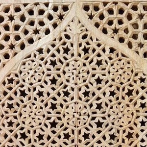 May include: Intricate wooden carving with a repeating pattern of stars and geometric shapes. The carving is light brown in color and has a smooth, polished finish.