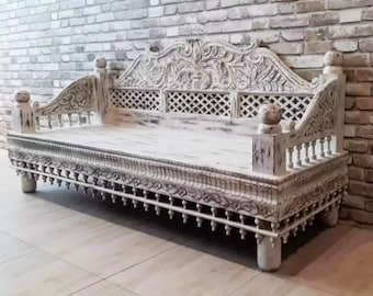 May include: Whitewashed wooden daybed with intricate carvings and a lattice design on the back. The daybed has a whitewashed finish and is decorated with beading around the bottom edge.