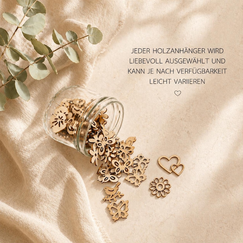 May include: A clear glass jar tipped on its side, spilling small, light-brown wooden cutouts in shapes of butterflies, flowers, birds, and hearts. The text JEDER HOLZANH&Auml;NGER WIRD LIEBEVOLL AUSGEW&Auml;HLT UND KANN JE NACH VERF&Uuml;GBARKEIT LEICHT VARIIEREN is visible.
