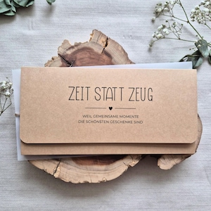 Könnte beinhalten: Ein rechteckiger Umschlag aus hellbraunem Kraftpapier mit einer Verschlussklappe. Auf der Vorderseite befindet sich der schwarze Aufdruck: ZEIT STATT ZEUG, gefolgt von einem kleinen Herzsymbol und dem Text: WEIL GEMEINSAME MOMENTE DIE SCHÖNSTEN GESCHENKE SIND.