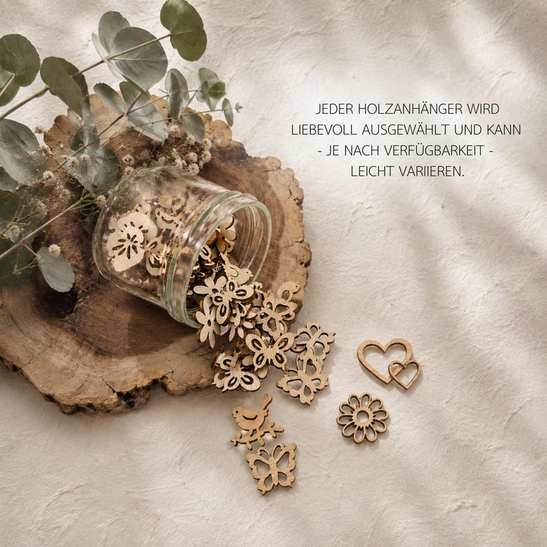 May include: A clear glass jar spilling out small, laser-cut wooden shapes including butterflies, flowers, birds, and hearts. The text JEDER HOLZANH&Auml;NGER WIRD LIEBEVOLL AUSGEW&Auml;HLT UND KANN - JE NACH VERF&Uuml;GBARKEIT - LEICHT VARIIEREN is printed on the right side.