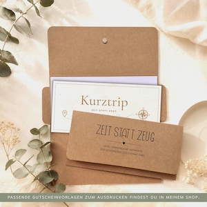 Pu&ograve; includere: Una busta in carta kraft marrone contenente un buono regalo bianco. Il buono riporta il testo "Kurztrip" e "ZEIT STATT ZEUG" con un grafico a bussola. Anche la patta della busta &egrave; stampata con "ZEIT STATT ZEUG" e una piccola icona a cuore.