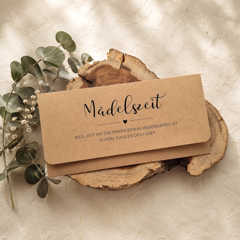 May include: A rectangular light brown kraft paper envelope featuring the black printed text M&auml;delszeit, a small heart icon, and the German phrase WEIL ZEIT MIT DIR IMMER ETWAS BESONDERES IST. SCH&Ouml;N, DASS ES DICH GIBT! The envelope rests on a wood slice.