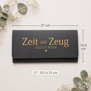May include: A rectangular black gift voucher envelope featuring gold foil text that reads Zeit statt Zeug GUTSCHEIN with a small heart icon. The envelope measures 8.27 inches by 4.13 inches as indicated by the visible dimension markers.
