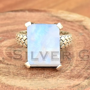 Puede incluir: Un anillo de plata con una piedra de luna rectangular engastada en una banda texturizada.