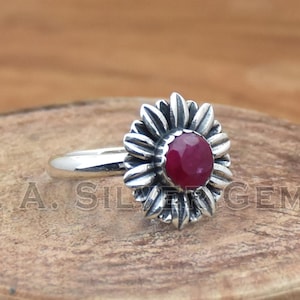 May include: A silver ring with a red gemstone set in a flower design.