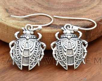 May include: A pair of silver earrings featuring a detailed beetle design. The earrings have a hook closure.