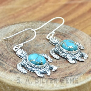 Peut inclure: Boucles d'oreilles en argent sterling avec une pierre turquoise sertie dans un motif de tortue détaillé. Les boucles d'oreilles ont une fermeture à crochet.