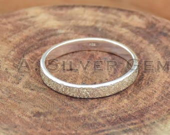 Könnte beinhalten: Ein silberner Ring mit strukturiertem Band, der auf einer Holzoberfläche liegt. Der Ring hat ein schlichtes, elegantes Design. Der Text "S. A. SILVER GEMS" ist auf der Holzoberfläche sichtbar.