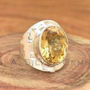 May include: A silver ring featuring a large, oval-shaped, yellow citrine gemstone. The ring has a textured band and a raised setting for the stone.