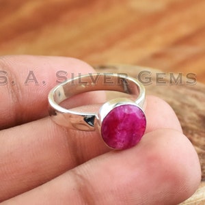 May include: A silver ring featuring a pink ruby gemstone. The ring has a plain band and the ruby is round and faceted.