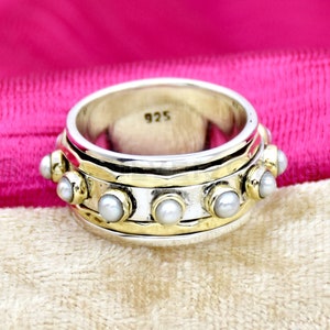 May include: A silver and gold ring with a row of white pearls around the band. The ring is marked "925" on the inside.