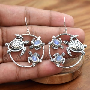 Può includere: Orecchini in argento sterling con un design circolare decorato con tre ciondoli a forma di tartaruga e pietre preziose di pietra di luna.