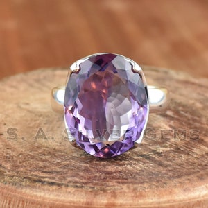 May include: A silver ring with a large oval amethyst gemstone. The ring is set in a simple, elegant style.