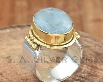 May include: A silver and gold ring with a large, light blue aquamarine gemstone. The ring has a textured band and a gold setting.