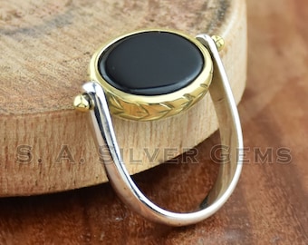 Könnte beinhalten: Ein Silber- und Goldring mit einem schwarzen Onyxstein. Der Stein ist in einer goldenen Fassung gefasst und der Ring ist drehbar.