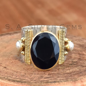 May include: A silver ring with a black gemstone and two white pearls. The ring has a gold band with a textured design.