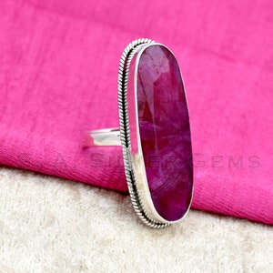 May include: A silver ring with a large, oval-shaped, pink gemstone set in a silver bezel. The ring has a decorative, twisted silver band.