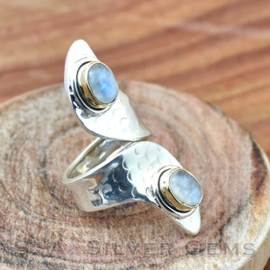 May include: A silver ring featuring two moonstone gemstones set in gold. The ring is designed in a curved, open shape.