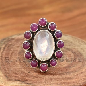 May include: A silver ring featuring a large oval moonstone set within a halo of smaller pink gemstones.