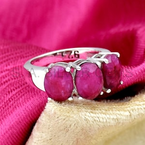 Op de afbeelding: Een zilveren ring met drie roze edelstenen. De ring is gemarkeerd met het nummer "925" aan de binnenkant van de band.