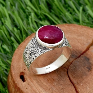 Pode incluir: Um anel de prata com uma banda texturizada e uma grande gema de rubi de forma ovalada engastada em um engaste de bezel.