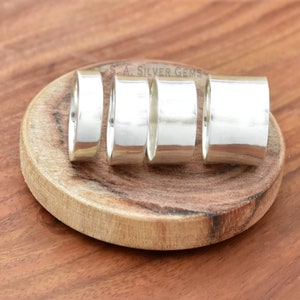 May include: Four silver rings of varying widths, arranged in a row on a wooden surface. The rings are smooth and polished, with a shiny finish. The text "S.A. SILVER GEMS" is visible in the background.