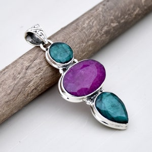 May include: A silver pendant with three gemstones. The top and bottom stones are green, and the middle stone is a large, oval-shaped, pink gemstone.