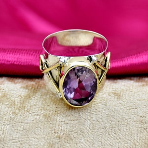May include: A silver and gold ring featuring a large oval amethyst gemstone. The ring has a textured band with a twisted design.