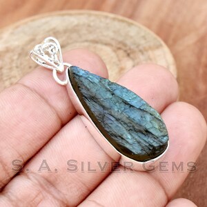 May include: A silver pendant featuring a teardrop-shaped labradorite gemstone with a dark blue and green iridescent sheen. The pendant has a delicate, intricate silver bail.
